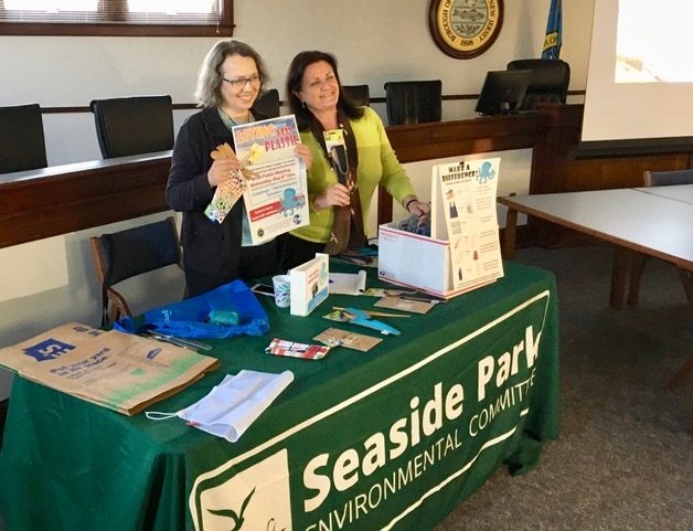 Two women stand behind a table displaying a sign that reads Seaside Park, smiling and engaging with visitors